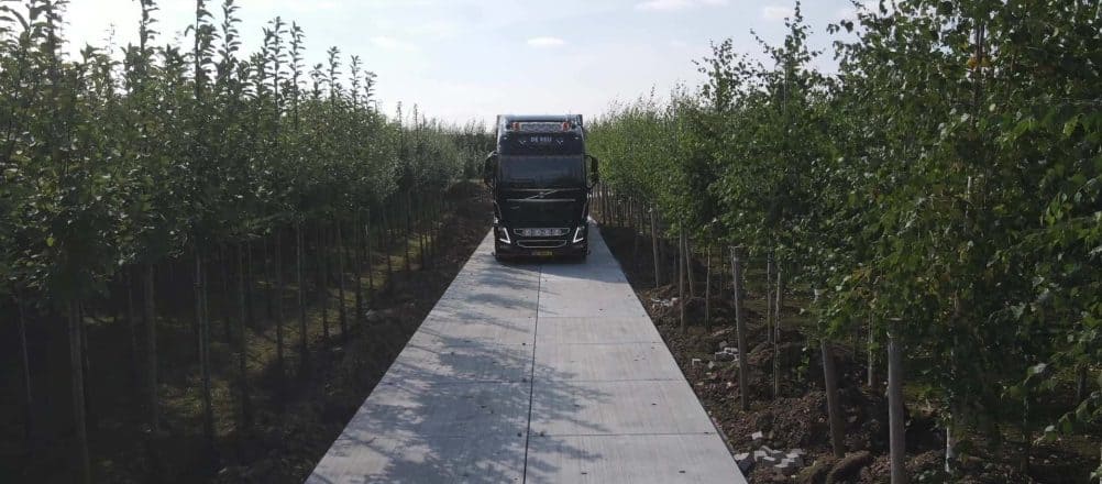 Vrachtwagen van De Keij die over een betonplaten pad rijdt in een boomgaard